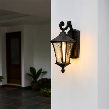Black metal outdoor lantern with textured glass and curved arm glowing warmly on a white exterior wall creating an elegant inviting entrance ambience.