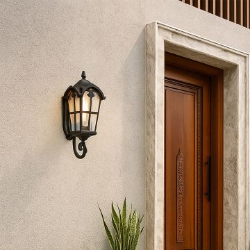 Classic black metal outdoor lantern with light on mounted beside a wooden door adding warm illumination and elegant detailing to the exterior wall.