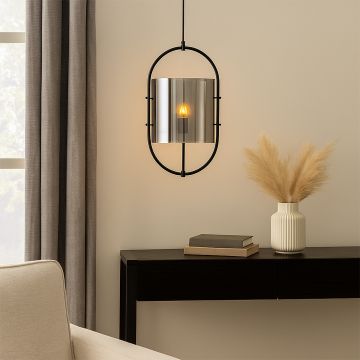 Modern pendant light with a black oval frame and tinted chrome glass shade softly glowing hanging above a console table styled with books and a vase.