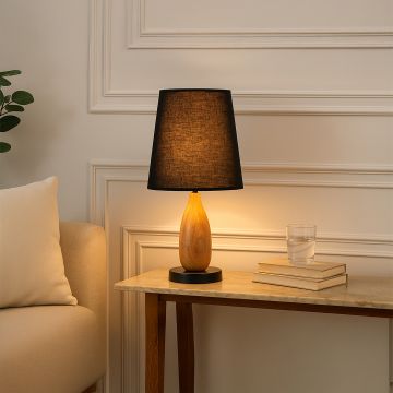 Modern table lamp with tall black fabric shade natural wooden sculpted body and smooth metal base adding warm ambient lighting to contemporary interior home decor.