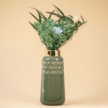 A tall green ceramic vase with a glossy finish and gold rim displayed with lush green florals on a warm beige background creating a soft lifestyle setting that highlights its elegant textured design.