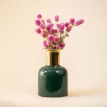 A green ceramic vase with a glossy finish and gold neck is styled with pink flowers on a soft beige background creating a warm and elegant lifestyle scene.