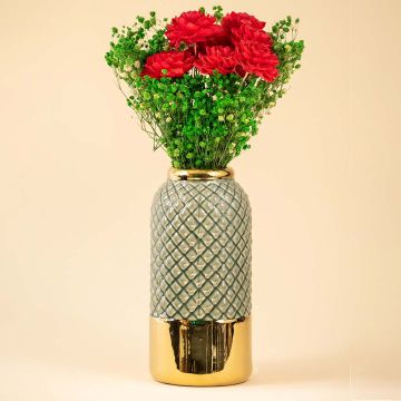 A tall textured grey and gold vase filled with vibrant red flowers placed against a soft beige interior background creating a warm lifestyle decor look.