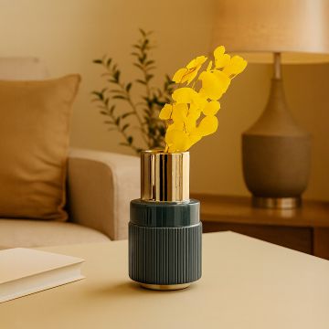 Modern ceramic vase with glossy gold top and ribbed blue base styled on a living room table creating a warm elegant decor accent with bright yellow flowers displayed.