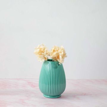 Stylish ribbed vase in green placed on pink marble surface beautifully enhancing home interior style.