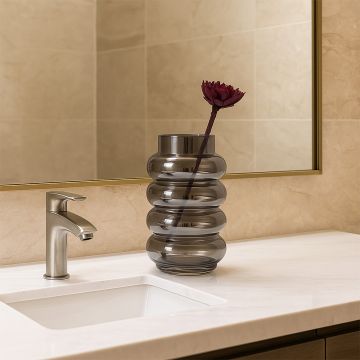 Smoky glass vase with wavy design placed on a marble countertop beside a sink mirror adding a modern touch to the bathroom decor.