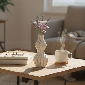 Wavy ceramic vase styled on a wooden coffee table with lavender and pink blooms beside a steaming cup in cozy daylight setting.