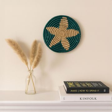 Medium beige and teal woven wall basket hanging on a white wall above a wooden console with dried flowers for modern boho decor.