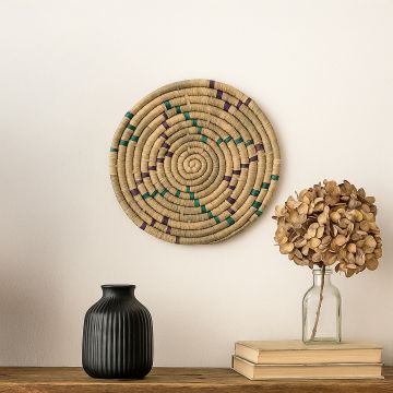 A teal mustard and natural woven rattan wall decor plate displayed in a bright room setting beside decorative accents adding vibrant artisan texture to modern interior decor.