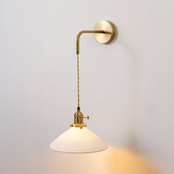 Gold metal wall light with white ribbed shade glowing softly on white background for elegant vintage inspired home decor.