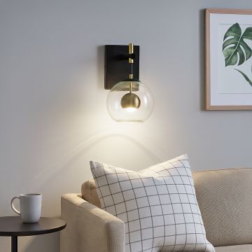 Modern black wall sconce with clear glass globe and brass gold sphere accent mounted on interior wall creating elegant lighting.