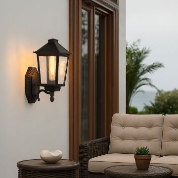 Black metal outdoor lantern with clear textured glass glowing warmly beside a patio seating area creating a cozy and elegant outdoor ambience.