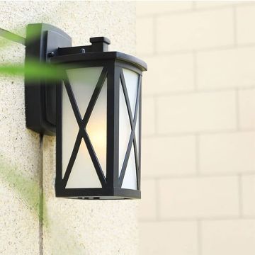 Black metal outdoor lantern with frosted glass and X frame design mounted on a textured exterior wall creating a warm modern outdoor ambience.