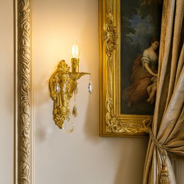 Golden wall light with crystal drops glowing in luxury interior beside classic painting and ornate curtain.