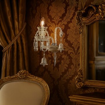 Crystal wall light glowing in luxury room with golden wallpaper ornate mirror and upholstered chair.