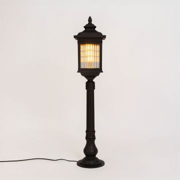 A contemporary black outdoor bollard light displayed against a white background with the light on showcasing its tall rectangular design and clear vertical glass panels with warm illumination.