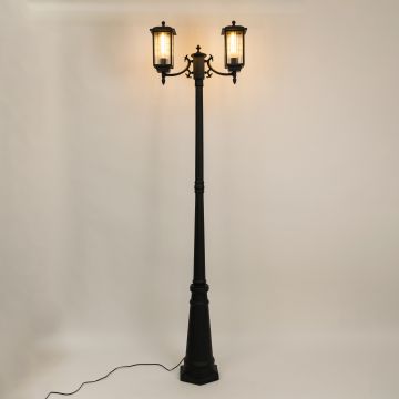 Black metal dual lantern outdoor lamp post light on with ribbed glass glow standing tall on white background ideal for driveway pathway and garden Decor.