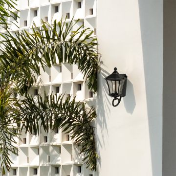 Black vintage outdoor wall lantern styled in a soft lifestyle setting with clear patterned glass and a warm glowing bulb for an elegant exterior look.