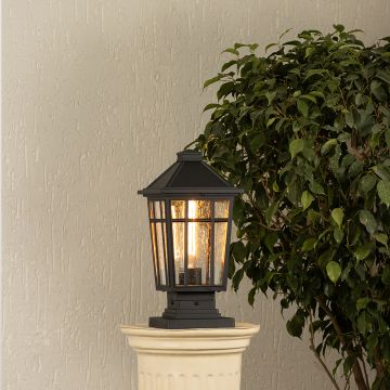 Black metal outdoor post lantern Light On mounted on a stone pillar Traditional garden gate lighting Main Lifestyle image at night.