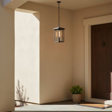 A modern black hanging lantern light glowing warmly at an outdoor entrance casting soft shadows on beige walls and creating a welcoming ambiance with a minimal front porch setting.