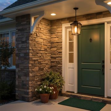 Black vintage hanging lantern with the light on illuminating a stone entrance wall and creating a warm inviting glow at the front door for classic outdoor home styling.