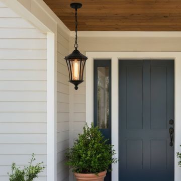 A classic black hanging outdoor lantern with warm light turned on illuminating a modern porch near a blue front door creating a welcoming ambience at the entrance at night.