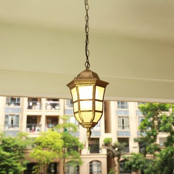 Black metal outdoor pendant light hanging on a porch ceiling with warm light on creating an inviting glow against a blurred apartment background.