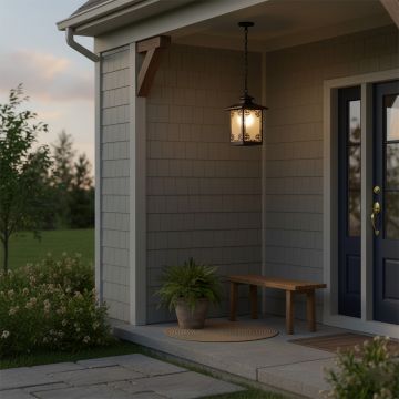 A warm outdoor porch scene at dusk featuring a hanging lantern light that is turned on casting a soft glow near the entryway with plants a bench and a doormat creating a welcoming ambiance.
