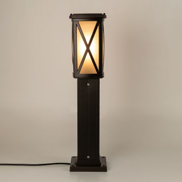 Black outdoor bollard light with frosted glass and X frame design glowing warmly and adding elegant ambient illumination to modern garden and pathway spaces.