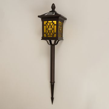 Brown solar garden spike lantern with patterned glass shown with light on against a white background highlighting its warm glow and ornate outdoor design.