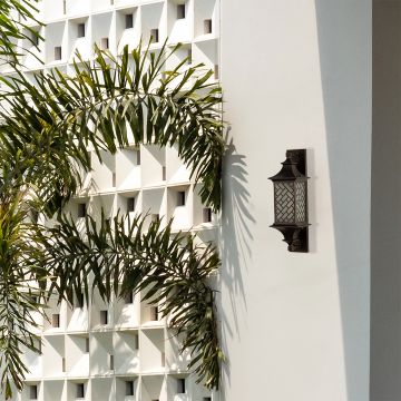 Tall brown metal outdoor lantern with light on mounted on a modern exterior wall creating warm illumination with decorative lattice glass for elegant outdoor decor.