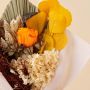 Detailed preserved bouquet closeup featuring orange infinity rose yellow apple leaves hydrangea pampas grass and lotus pod.