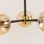 Close-up image of a modern chandelier with black metal rods and amber glass globes connected by a sleek golden center fixture.