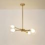 Gold sputnik chandelier with clear glass sphere shades turned off on white background showing mid-century modern fixture.