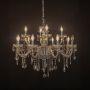 Crystal chandelier with candle lights and hanging crystal drops glowing warmly on black background view.