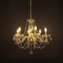 Crystal chandelier with gold detailing turned on against black background creating a warm radiant glow.