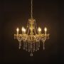 Gold chandelier with lights on glowing warmly with crystal beads and glass body against a black background.