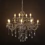 Black chandelier with lights on glowing warmly with crystal drops and glass arms against a black background.