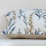 Closeup view of blue and gold botanical embroidery on a soft beige cushion capturing intricate threadwork texture and natural elegant home decor detailing.