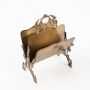 Top angled view of ornate brass tissue holder showing curved panels with vintage handle design on white base.