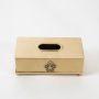 A gold tissue box with an ornate emblem shown on a white background highlighting its smooth metallic finish and simple rectangular structure.