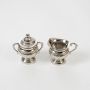Silver sugar pot and creamer set shown on a white background highlighting detailed engravings and smooth reflective finish for a clear product view.