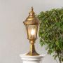 Classic golden pillar lamp glowing on stone pillar for outdoor entrance and pathway lighting with stylish home garden design.