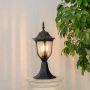 Outdoor black pillar lamp glowing warmly on a stone pillar adding timeless charm to garden gate and home entrance lighting.