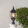 Black metal outdoor pillar lamp glowing with curved glass shade placed on stone pillar ideal for garden and patio decor.