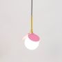Pendant light with pink shade gold finish and frosted glass globe glowing warmly on plain white background.