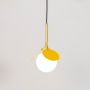 Pendant light with yellow frame and glowing frosted globe hanging lamp photographed on white background.