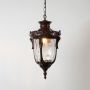 Antique brass hanging lantern glowing on white background showcasing intricate carved details and glass design.