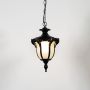 Black vintage hanging lantern light glowing on white background highlighting its frosted glass and ornate design.