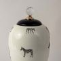 Closeup of white ceramic jar showing detailed black zebra artwork and glossy finish with elegant crystal knob top.